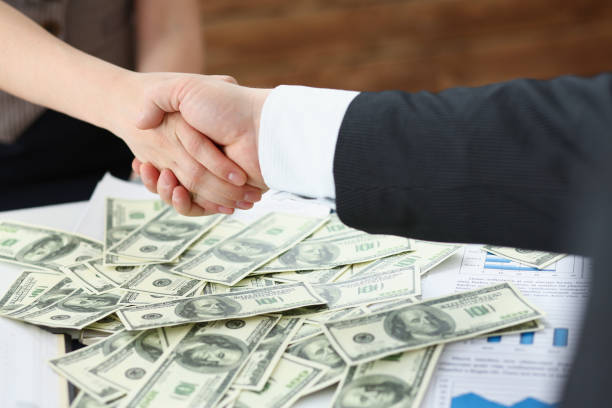 istock Man and woman shake hands over stack of dollars currency transaction of powers 1357838754