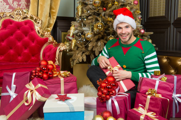 istock Man in santa hat with presents at Christmas tree 1357839499