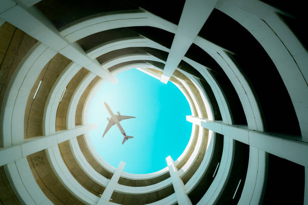 Bottom view multi-story car park building with plane flying above building. Air logistic. Aviation and travel business.  Architecture of spiral curve building. Airline business. Tourism transportation