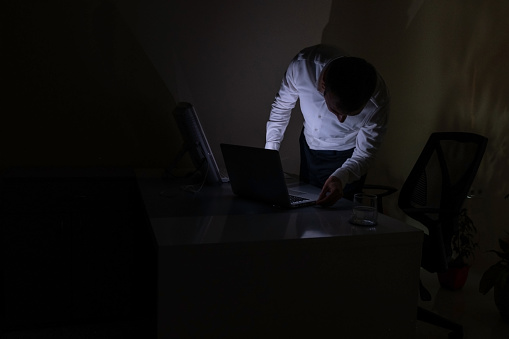 Young office worker aged 25-30 continues to work from a laptop when there is a power cut