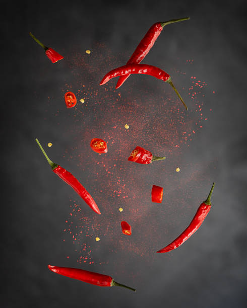 Flying hot red chili peppers with paprika powder against black background Levitation or flying of red chili pepper whole and slices with paprika powder used for food seasoning to make hot spicy flavour in mexican and asian cuisine against dark black background. Vertical chilli powder stock pictures, royalty-free photos & images