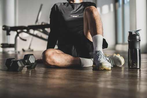 Young athlete wearing black sport wear exercise sitting on the floor in fitness center and stretching after strenuous exercise function training workout with personal trainer and healthy lifestyle.
