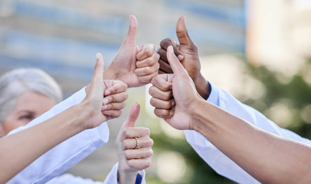 Shot of a group of unrecognizable doctors showing a thumbs up against a city background We're doing a great job as healthcare workers professional thank you stock pictures, royalty-free photos & images