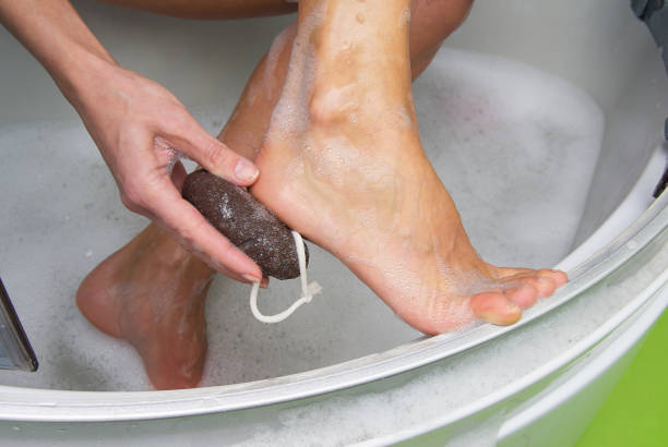Young woman exfoliating her dry skin heel with a natural pumice stone. stock photo