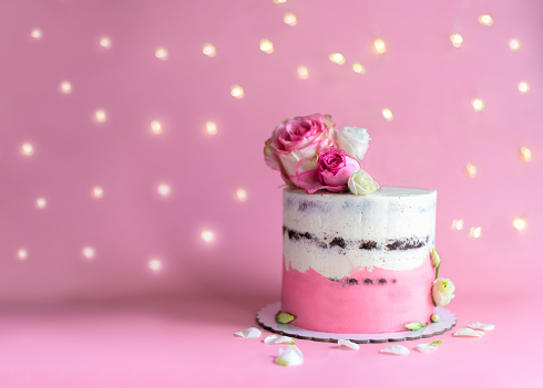 Pink cake decorated with natural roses on a pink background with bokeh lights. Selective focus
