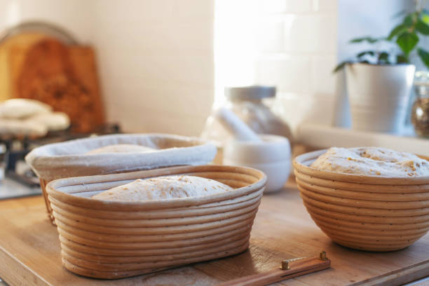 os preparos do pão sourdough em cestas de rattan rasstoechnye estão na mesa . a garota faz incisões com uma faca e coloca no forno para assar. - lifestyles domestic kitchen human hand furniture - fotografias e filmes do acervo