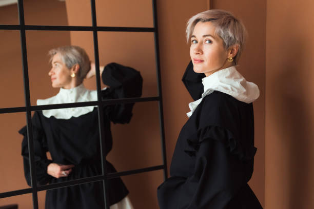 modefrau in vintage schwarz-weiß kleid stehendem braunem hintergrund blickend in die kamera - jabot stock-fotos und bilder