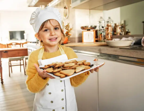 Photo of Proud Little girl cook portrait holding homemade cookies in a domestic kitchen