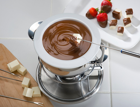 Classic chocolate fondue pot, with cheese and strawberries on skewers.