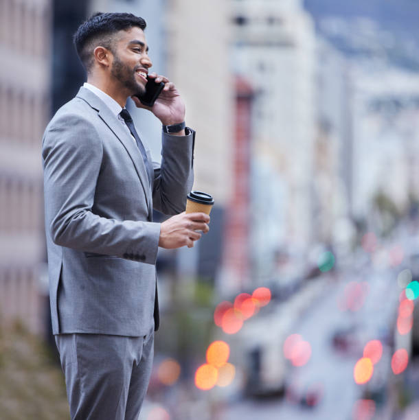 istock Shot of a handsome young businessman standing alone and using his cellphone while enjoying a cup of coffee 1357867353
