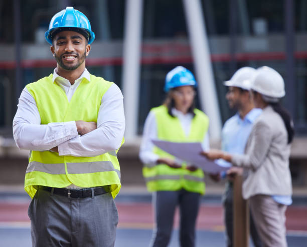 istock Shot of a handsome young architect standing with his arms folded while his colleagues discuss behind him 1357867382
