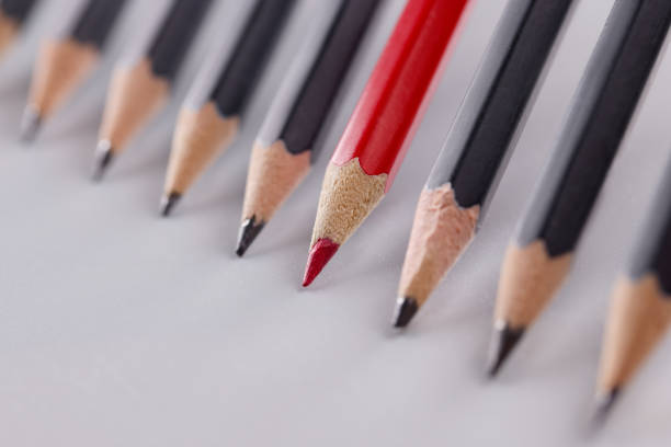 istock Red pencil that stands out from many identical black pencils on gray background 1357867577