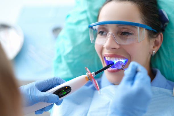 zahnarzt arbeitet mit dentalpolymerisationslampe in der mundhöhle - freundschaftliche verbundenheit stock-fotos und bilder