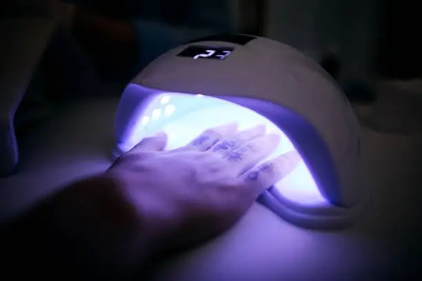 Customer puts his hand in the dryer with a UV lamp in a beauty salon