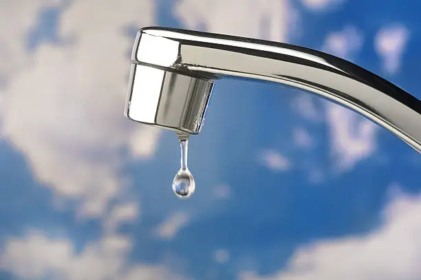 Photo of Single water drop from stainless faucet; clouded blue sky background