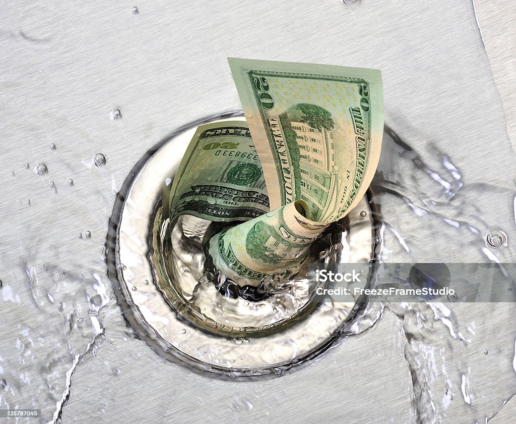 Wasted money going down the sink drain US currency going down a stainless steel sink drain. $20 bills with water in spiral vortex Money Down the Drain Stock Photo