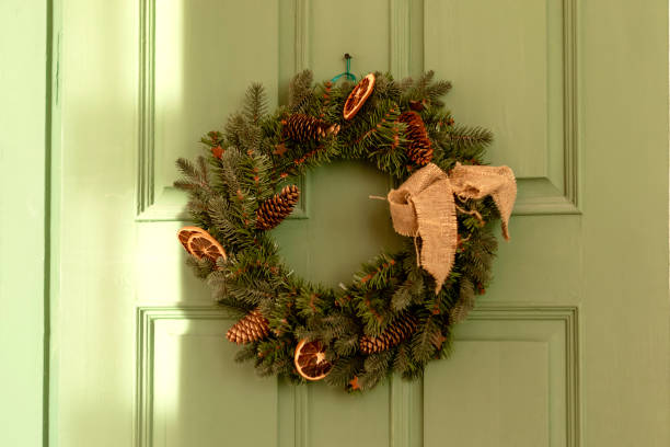 Festive Christmas wreath made of fir branches on a green wooden door.The wreath is decorated with cones, dried lemon slices and a burlap bow.New Year, Christmas and eco-friendly concept stock photo