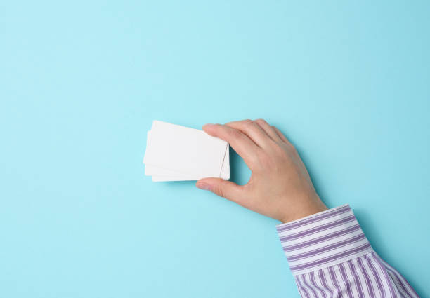 istock Female hand holding empty paper white business card on a blue background. Copy space 1357873123