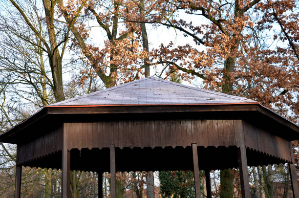 polygonal pergola with benches and a fence around the perimeter. there is a lot of space inside. the roof is pyramidal covered with asphalt shingles, in natural park, footpath, gravel polygonal pergola with benches and a fence around the perimeter. there is a lot of space inside. the roof is pyramidal covered with asphalt shingles, in natural park, footpath, gravel heptathlon stock pictures, royalty-free photos & images