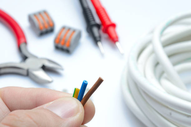 istock stripped, electrical three-core wire in hand against the background of terminal blocks and tools. close-up. 1357875551