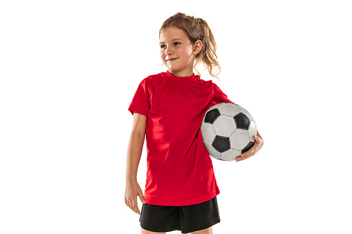 Girl, child, football player in red uniform holding ball and posing isolated over white background. Concept of action, sportive lifestyle, team game, health, energy, vitality. Copy space for ad