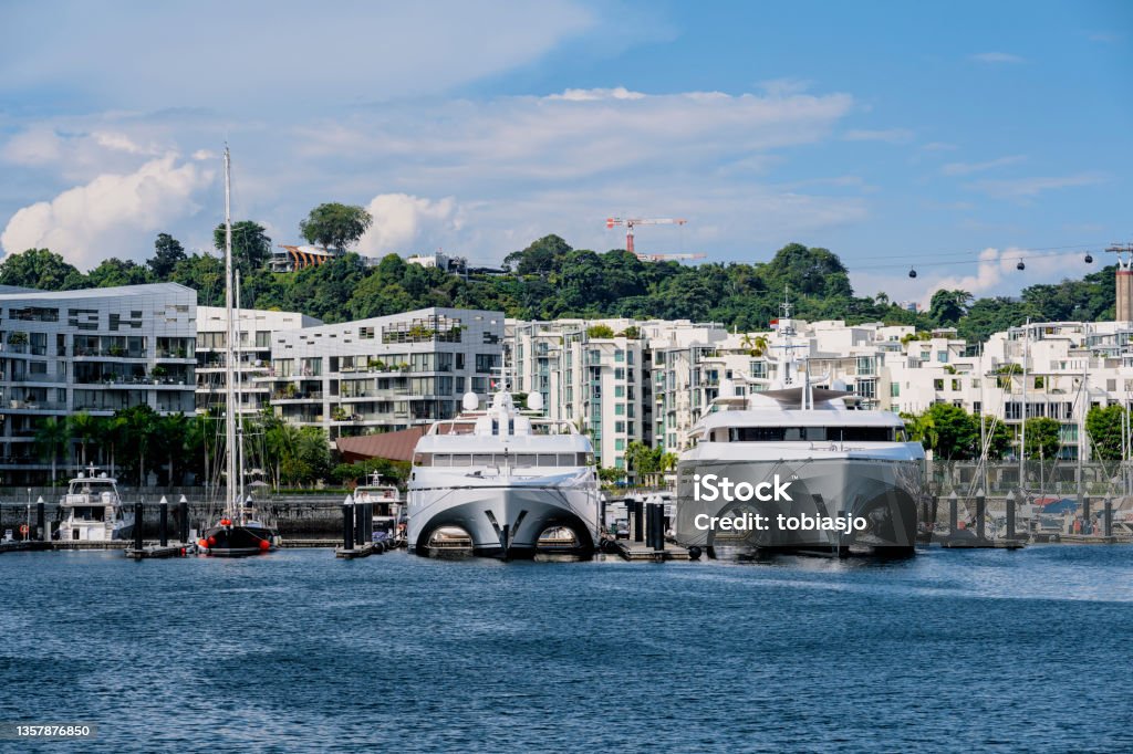 Singapore yacht marina and luxurious smart homes Modern residential area in Singapore full of yachts parked in the marina. People live in small compact smart home apartments close to the neighbour, but yet surrounded by lush green tropical rainforest and ocean water. This aerial view shows the Keppel Bay area in the southern tip of Singapore. Singapore Stock Photo