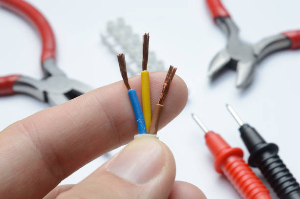 istock stripped, electrical three-core wire in hand against the background of terminal blocks and tools. close-up. 1357878418