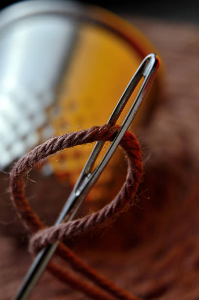 istock sewing needle with thread inserted into it. against the background of a large bobbin of thread and a thimble. close-up. 1357878976
