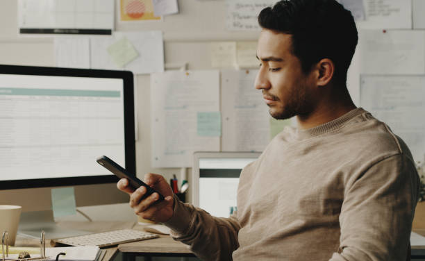 istock Shot of a handsome young businessman sitting alone and looking contemplative while using his cellphone in his home office 1357881560