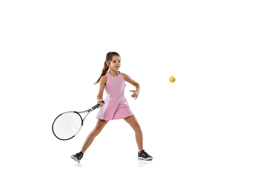 In action. Portrait of one little sportive girl, beginner tennis player palying tennis isolated on white studio background in neon light. Sport, study, childhood concept. Copy space for ad, text.