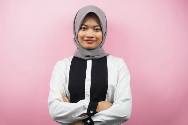 Beautiful young asian muslim woman smiling confidently with arms outstretched facing the camera isolated on pink background stock photo