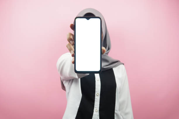 Muslim woman with hands holding smartphone, presenting app, presenting something, isolated on pink background, advertising concept stock photo
