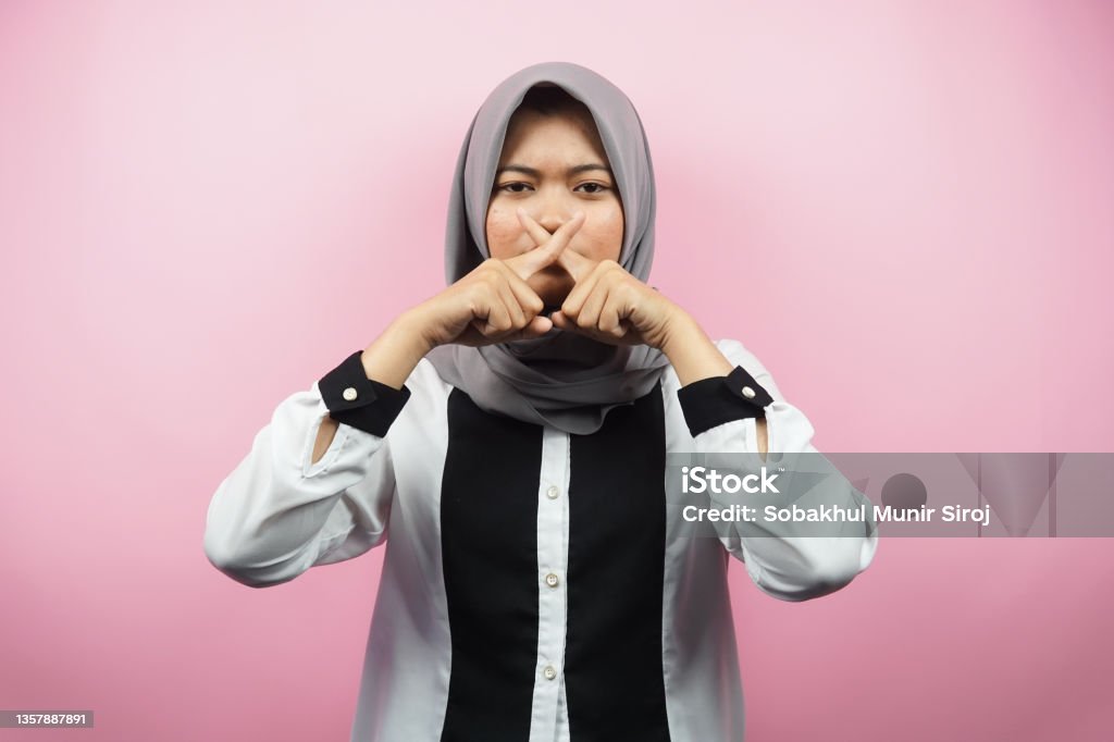 Beautiful asian young muslim woman with finger on mouth, telling to be quiet, don't make noise, lower your voice, don't talk, isolated on pink background 20-24 Years Stock Photo