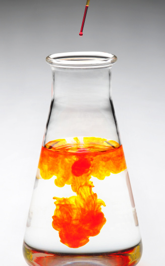 Titration tube dropping orange drops into a clear beaker. Dramatic plume, sharp and saturated throughout.
