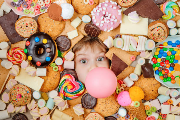 kleines mädchen, das unter vielen süßen speisen liegt - ungesunde ernährung stock-fotos und bilder