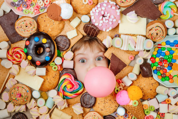 甘い食べ物の多くの下に横たわっている小さな女の子 - little cakes ストックフォトと画像