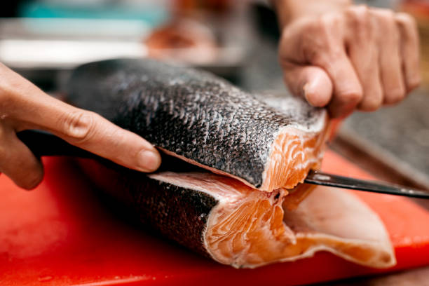 The chef's hand cutting a salmon on a cutting board with a knife stock photo