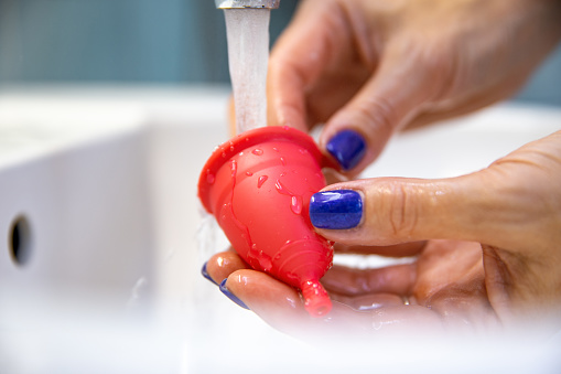 Mujer lavando una copa menstrual de silicona en el lavabo de un baño photo