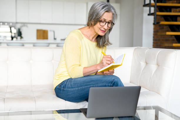 istock Focused mature mid-age gray-haired woman in glasses using laptop 1357899505