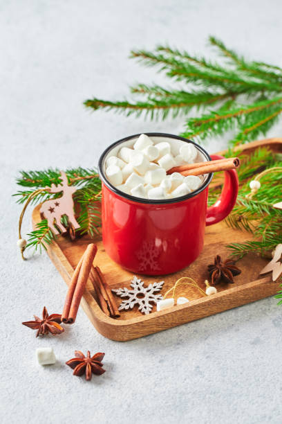istock Red cup of hot cocoa with marshmallows and candy canes on with christmas tree 1357899551
