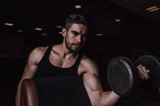 istock Muscular man working out in gym doing exercises with dumbbells at biceps 1357902972