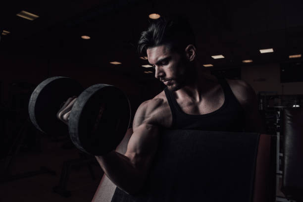 istock Muscular man working out in gym doing exercises with dumbbells at biceps 1357903575