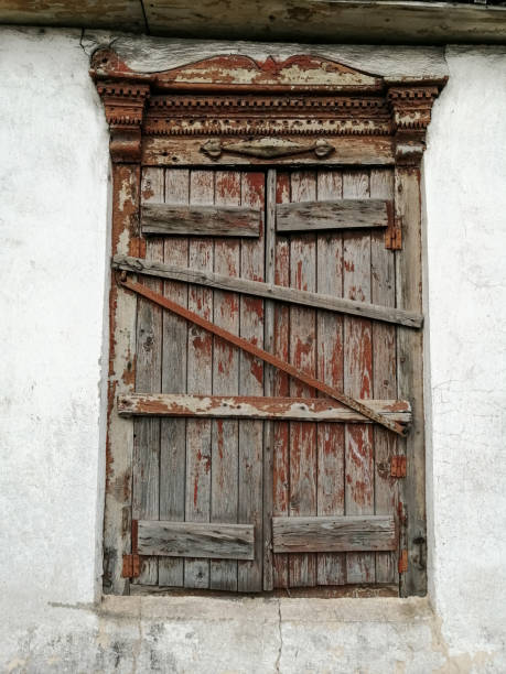 the old window with peeling red is boarded up with wooden beams. - mullion windows imagens e fotografias de stock