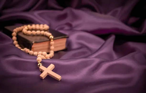 Closeup of wooden Christian cross on bible and prayer beads on black.Church utensils.