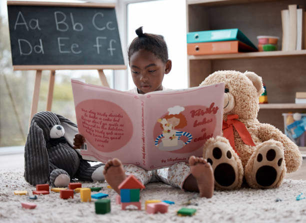 Shot of an adorable little girl reading a book while sitting at home Even my toys like it when I take this book out picture book stock pictures, royalty-free photos & images