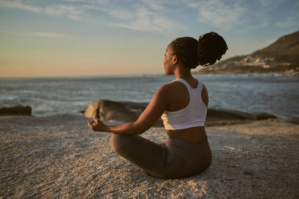 foto de cuerpo entero de una atractiva joven practicando yoga en la playa - meditating fotografías e imágenes de stock
