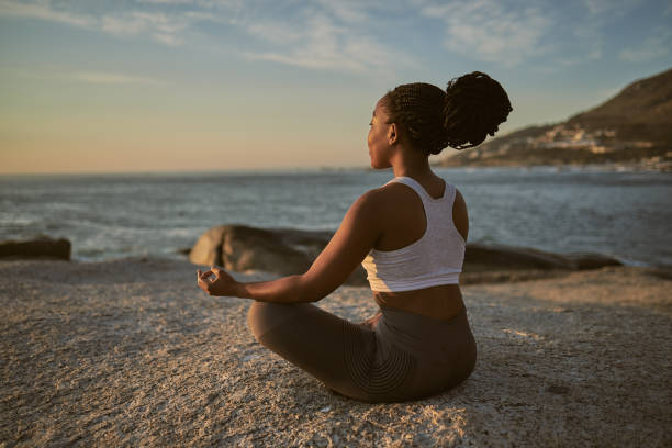 tiro completo de uma jovem atraente praticando yoga na praia - meditating - fotografias e filmes do acervo