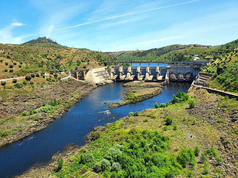 Photo of a dam in a portuguese river in Alentejo, Portugal, surrounded by a large area of vegetation.