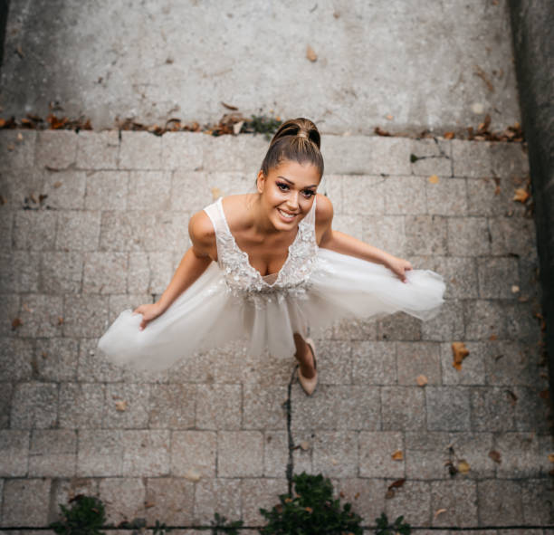 International wedding.Caucasian bride with white skin and long dark hair in a beautiful white dress holding a bouquet stands with her stylish Indian groom in a black suit and bow tie. Floral arch, wedding chairs, and sea view.