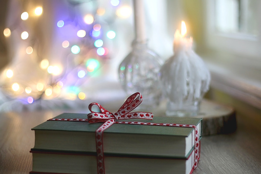 Two hardcover books wrapped with festive ribbon. Colorful Christmas lights in the background. Giving books for Christmas. Selective focus.